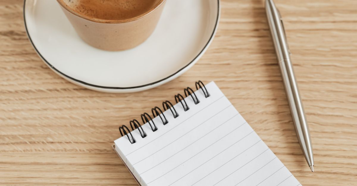 Notebook, pen and coffee arranged on a sunlit desk for morning planning